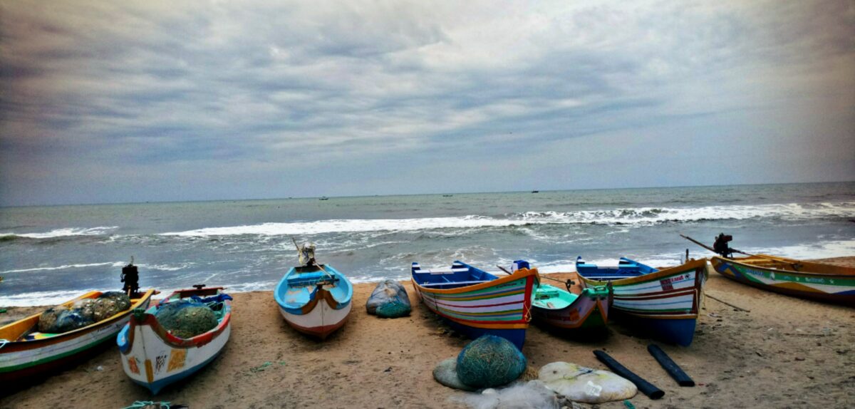 Bunte Fischerboote am Strand vor wolkigem Himmel.
