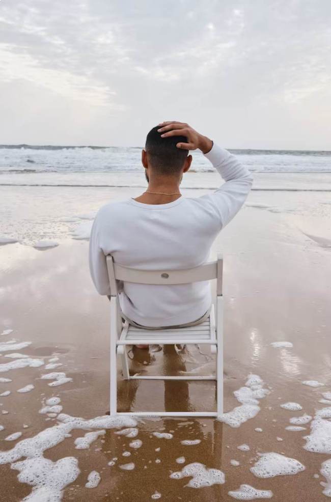 Ein Mann sitzt auf einem weißen Stuhl in der Brandung und blickt aufs Meer