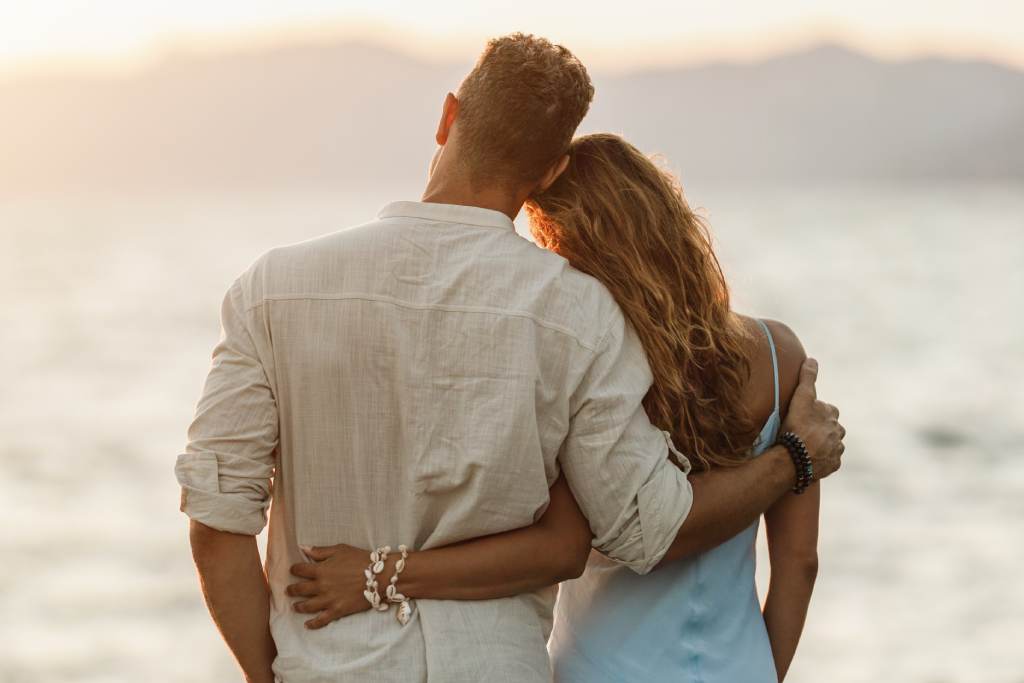 Ein Paar steht Arm in Arm und blickt auf das Meer im Abendlicht